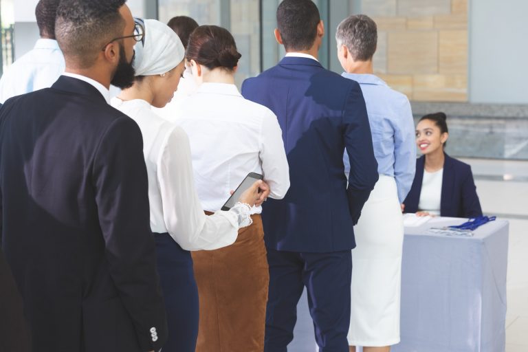 Rear view of diverse business people checking in at conference registration table in office lobby